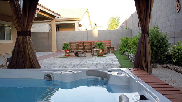 A hot tub in a backyard with a wooden deck, potted plants, and a brick wall. - Spacious Buckeye Vacation Home (Buckeye)