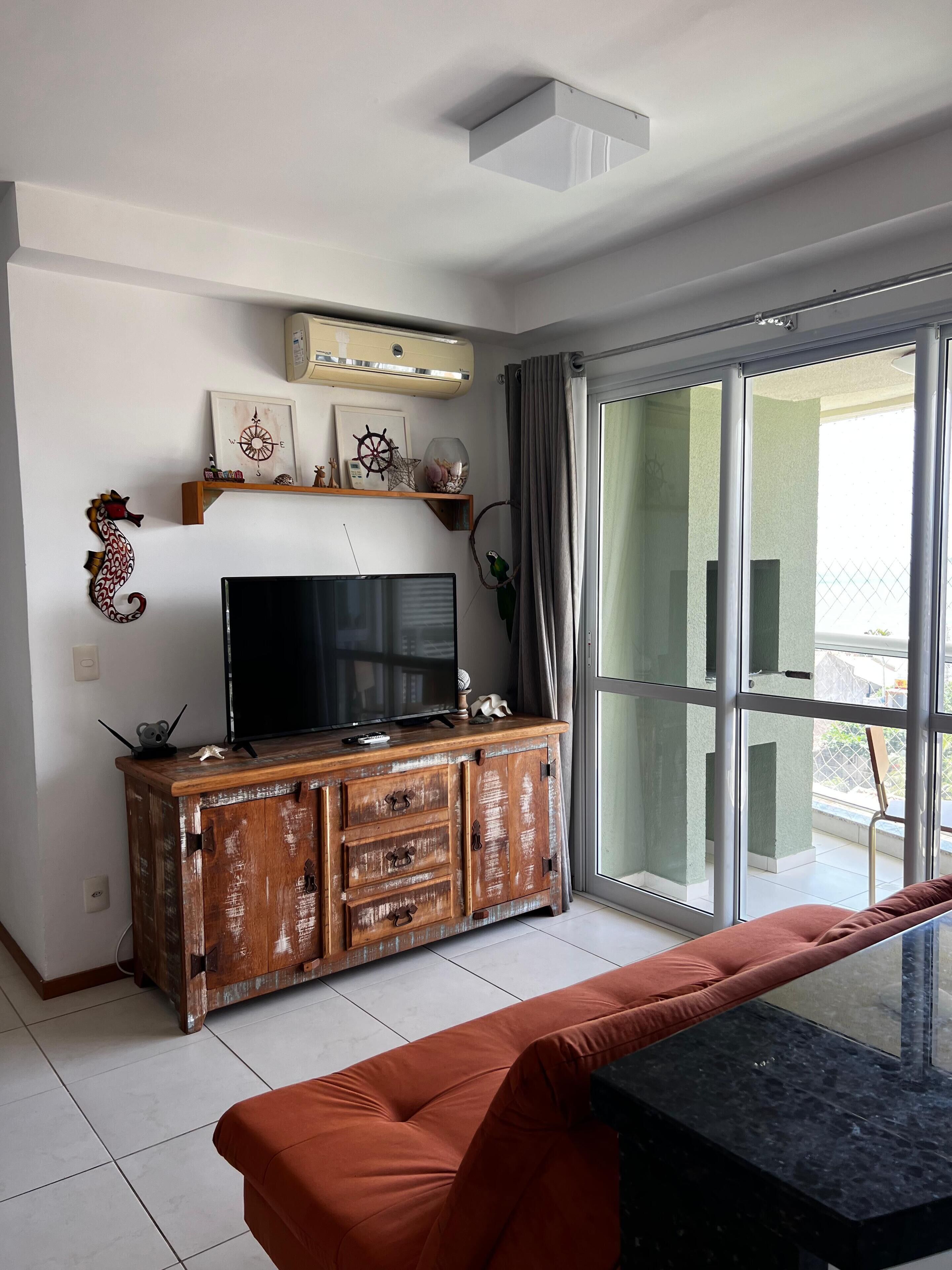 A modern living room with a flat-screen TV on a wooden cabinet, a red sofa, and a glass door leading to a balcony.