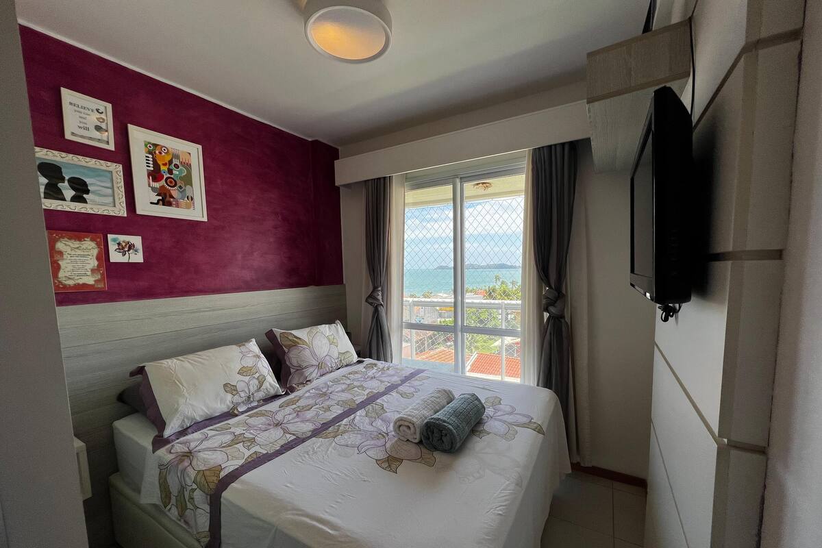 Quarto de hotel com cama, televisão e vista para o mar.