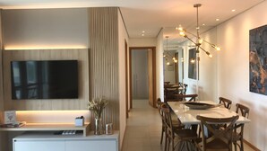 Een moderne woonkamer met een flatscreen televisie, een eethoek met houten stoelen, en een grote spiegel die de kamer weerspiegelt.