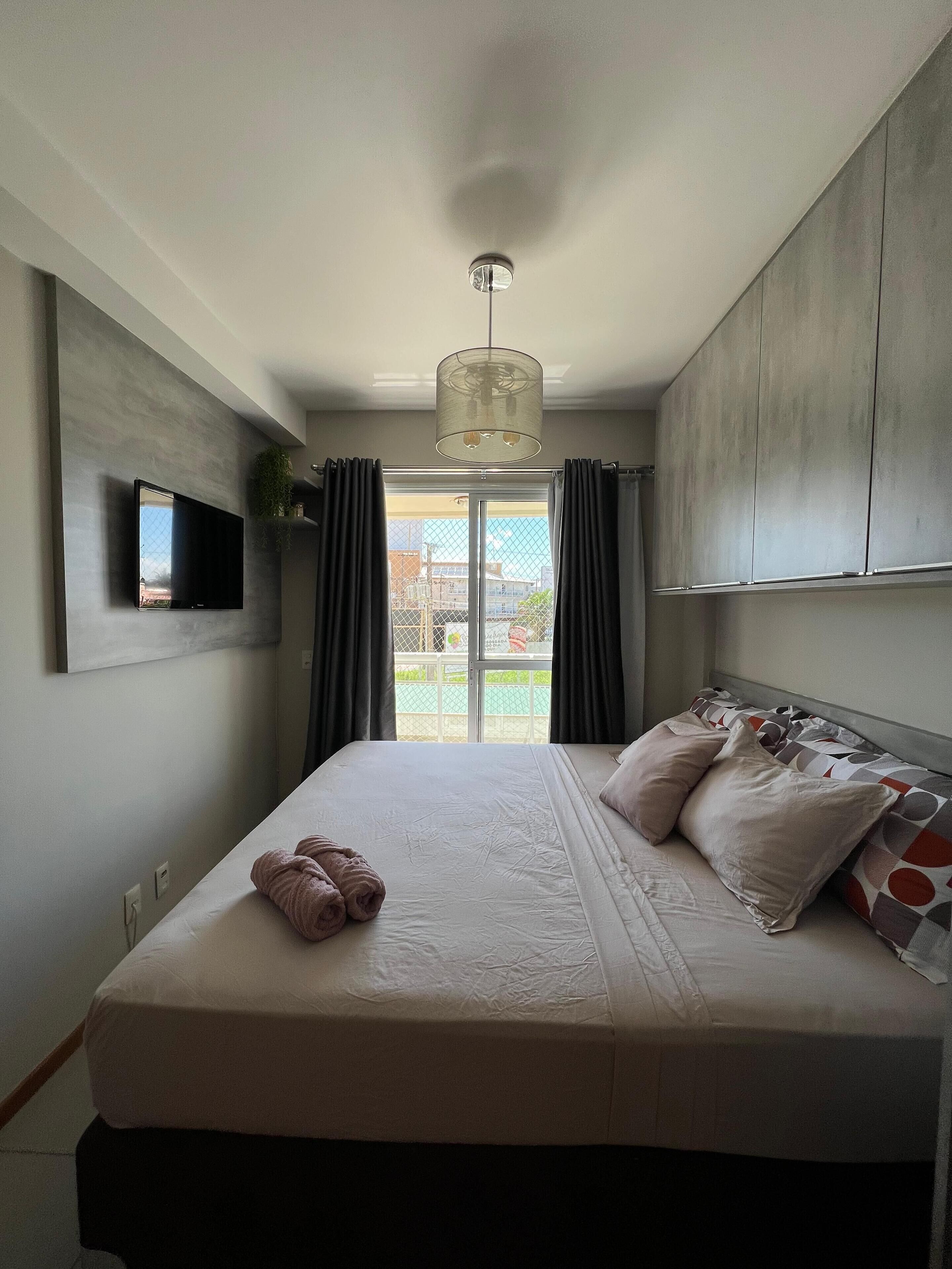 Een moderne slaapkamer met een groot bed, een flatscreen televisie aan de muur en uitzicht op het groen via een schuifdeur.