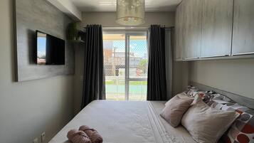 Een moderne slaapkamer met een groot bed, een flatscreen televisie aan de muur en uitzicht op het groen via een schuifdeur.