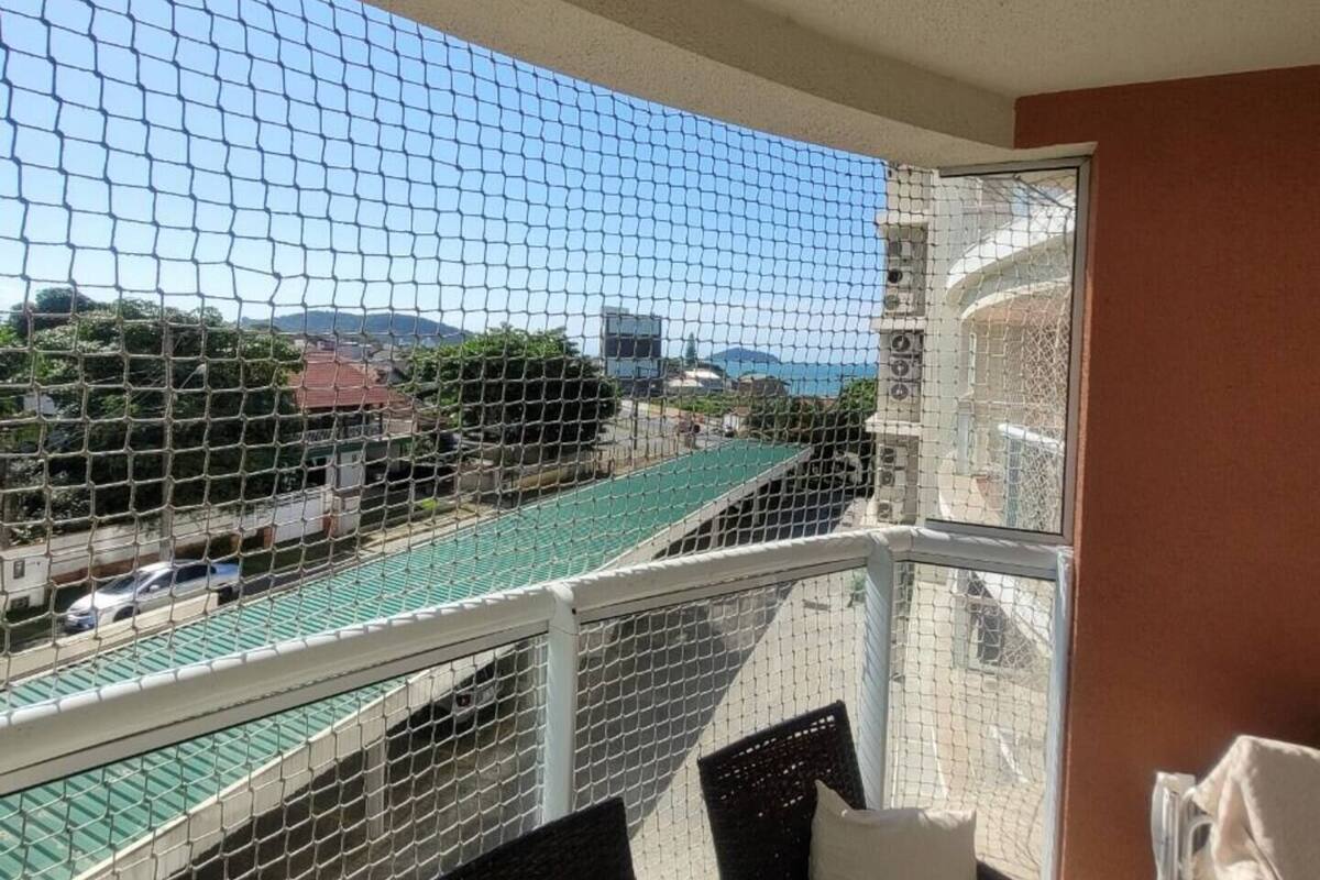 Uma varanda com cadeiras e almofadas de vime, com vista para uma rua com uma ponte verde e edifícios ao longe.