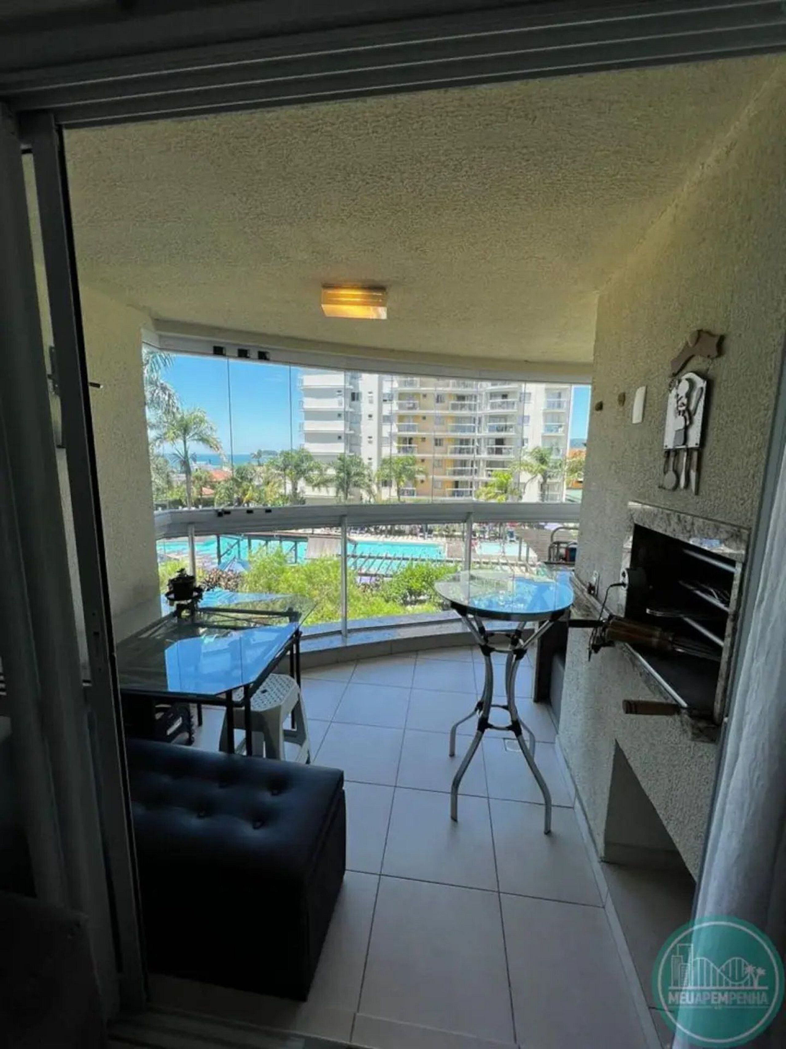 Un balcon avec une table et des chaises en verre, un barbecue et une vue sur une piscine et des immeubles.