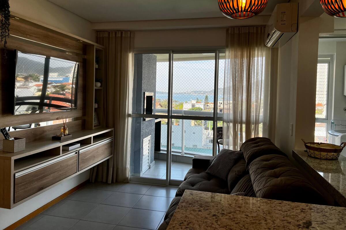 Uma sala de estar moderna com uma televisão de tela plana grande, um sofá confortável e uma varanda com vista para a cidade.