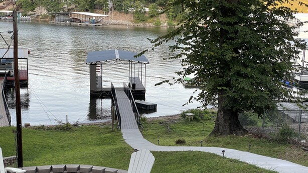Um deck à beira do lago com cadeiras Adirondack, uma lareira e um píer que se estende sobre a água.