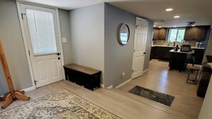 Uma sala de estar ampla com um tapete grande, um banco e vista para a cozinha.