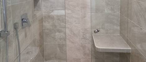 A modern shower area with a glass enclosure, a handheld showerhead, a wall-mounted faucet, and a shelf for toiletries.