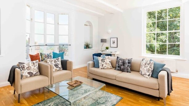 Ein geräumiges Wohnzimmer mit zwei Sofas, einem Glastisch und großen Fenstern mit Blick auf Grünflächen.