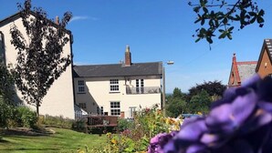 A white house with a black roof, surrounded by a well-maintained garden with various flowers. - Malvern Wells Apartment with Lovely Balcony Views (Malvern)