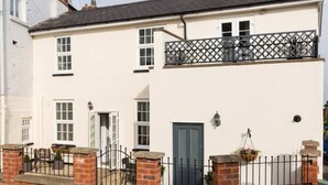 A two-story house with a white exterior, a black door, and a small balcony with a lattice railing. - Malvern Wells Apartment with Lovely Balcony Views (Malvern)