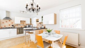 A modern kitchen with white cabinets, a central island, and a dining area with a table and chairs. - Malvern Wells Apartment with Lovely Balcony Views (Malvern)