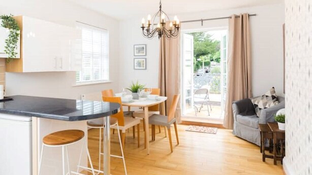 A modern kitchen with a central island, dining area, and a cozy seating space with a view of the outdoors. - Malvern Wells Apartment with Lovely Balcony Views (Malvern)
