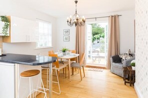 A modern kitchen with a central island, dining area, and a cozy seating space with a view of the outdoors. - Malvern Wells Apartment with Lovely Balcony Views (Malvern)