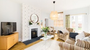 A living room with a fireplace, striped sofas, a TV on a wooden cabinet, and a hanging light fixture. - Fabulous 3 Bed Apartment with Private Courtyard (Malvern)