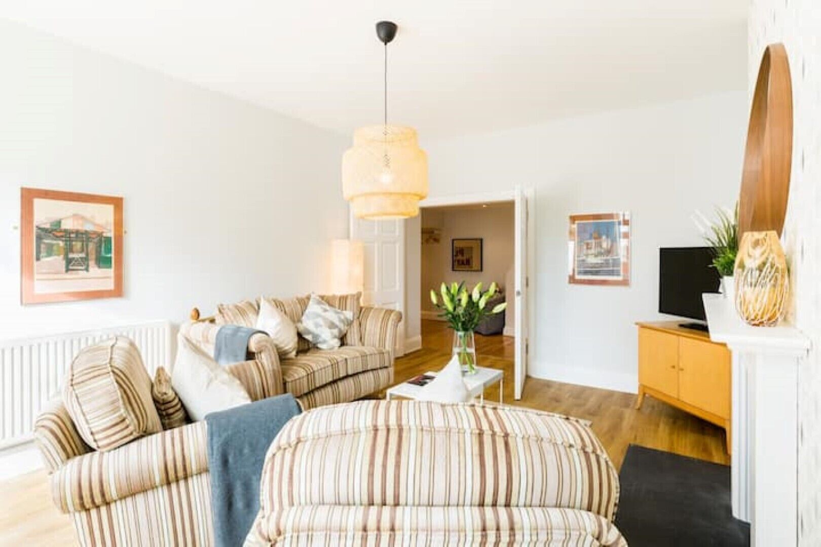 Een woonkamer met gestreepte banken, een salontafel, een televisie en een houten kast.