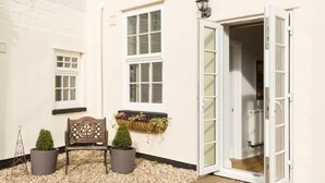 A white building with a wooden bench, two potted plants, and a window with a hanging planter. - Fabulous 3 Bed Apartment with Private Courtyard (Malvern)