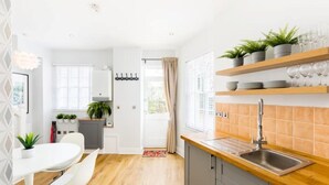 Een moderne keuken met een houten aanrecht, een spoelbak en een raam met zonwering. Er is een eethoek met een witte tafel en stoelen.