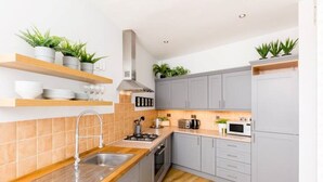 Een moderne keuken met grijze kastjes, een houten aanrechtblad en een roestvrijstalen spoelbak. Er staan planten op planken en een magnetron op het aanrecht.