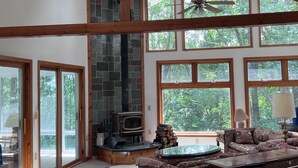 Amplia sala de estar con techo alto, ventanas grandes, chimenea y ventilador de techo.