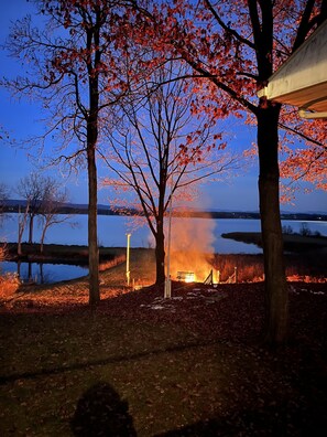 A serene outdoor setting with a fire, trees, and a body of water at dusk.