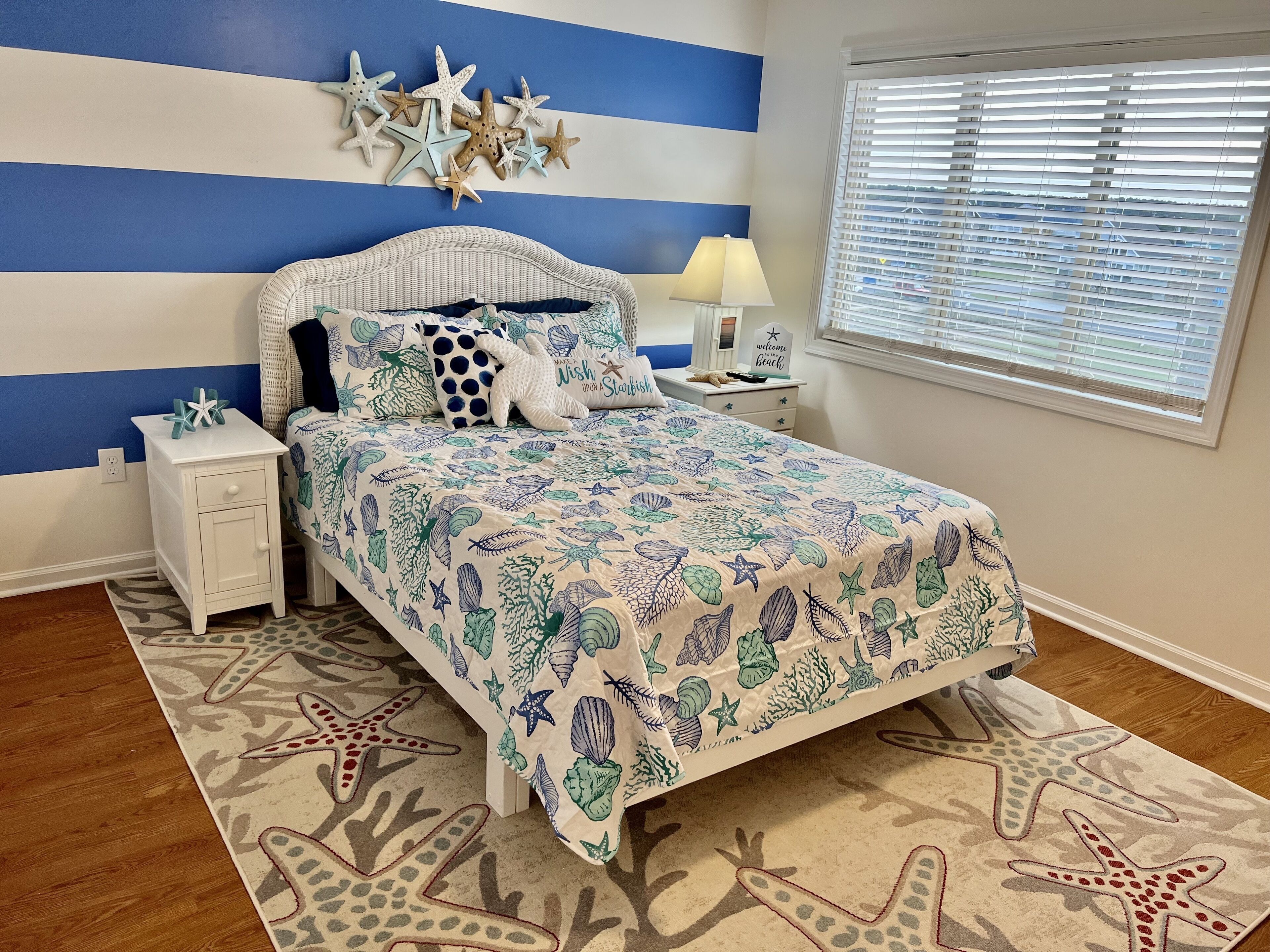 Un dormitorio con cama, mesitas de noche, una lámpara y decoración de estrella de mar en la pared.