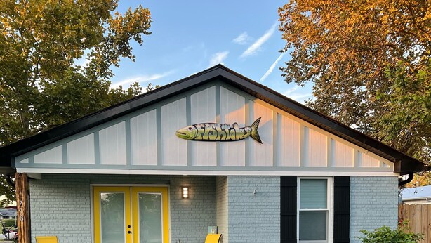 Une maison avec une enseigne en forme de poisson, une porte jaune et deux chaises à l’extérieur.
