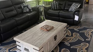Un salon avec deux canapés en cuir noir, une table basse en bois et un tapis à motifs.