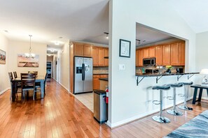A modern kitchen with wooden cabinets, stainless steel appliances, and a bar area with stools.