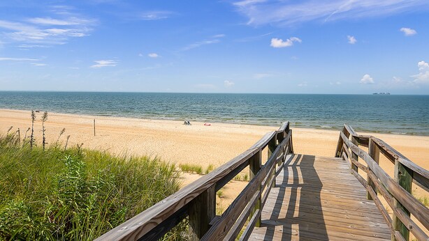 A wooden boardwalk leading to a sandy beach with clear blue water and a few boats in the distance. - Beachside Home • Fenced Yard • Dogs Welcome (Norfolk)