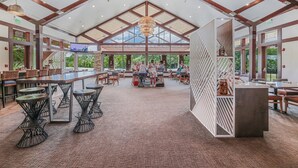 Un amplio espacio interior con techos altos, ventanas grandes y una variedad de disposiciones de asientos, incluyendo mesas y sillas.