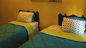 A room with two beds, each with a polka dot pillow and a quilted green and blue bedspread. There is a painting of a beach scene on the wall.