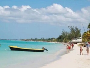 Une plage avec un bateau jaune, une eau turquoise et limpide, et des gens qui se promènent sur le sable.