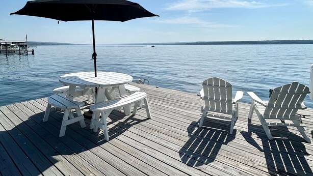 A wooden deck with a table and chairs, an umbrella, and a view of the water.