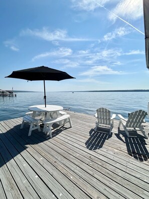 Una terraza de madera con una mesa, sillas y una sombrilla, con vista al agua.