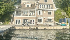 A multi-story waterfront house with a balcony, a dock, and a small boat.