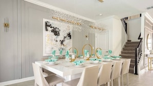 A dining area with a white table set for six, a staircase, and a large abstract painting on the wall. - 10BR Villa Near Disney, Pool and Resort Waterpark (Kissimmee)