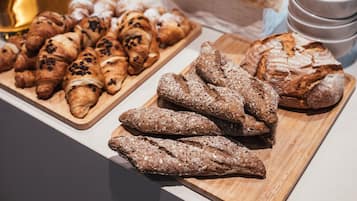 A buffet table with various breads and pastries, including croissants and baguettes, along with condiments and beverages.