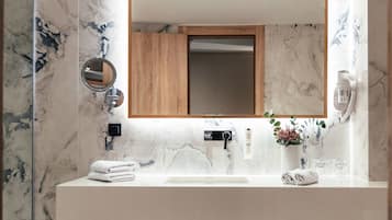 Une salle de bain avec un mur en marbre, un meuble en bois, un lavabo, un miroir et un porte-serviettes.