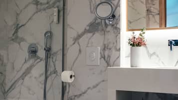 A bathroom with a marble wall, a toilet, a sink with a mirror, and a shower.