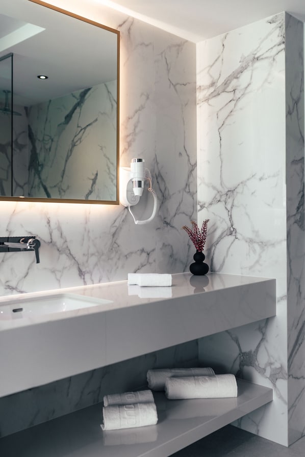 A modern bathroom with a marble backsplash, a large mirror, a white sink, and a towel rack with folded towels. - City Hotel Dubrovnik (Dubrovnik)