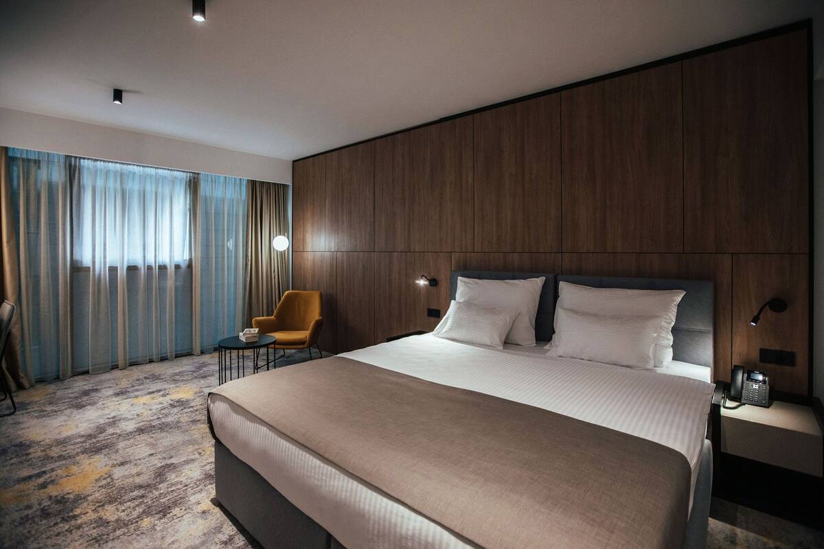 Ein Hotelzimmer mit einem großen Bett, einem Nachttisch mit Telefon, einem Sessel und einem kleinen Tisch.
