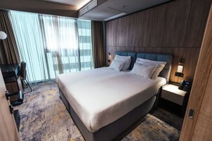Quarto de hotel com uma cama grande, uma escrivaninha e uma cadeira.