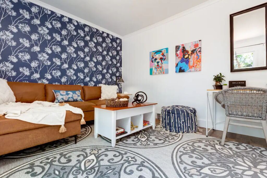 Un salon avec un canapé marron, une table basse blanche, un tapis à motifs et des œuvres d’art murales.