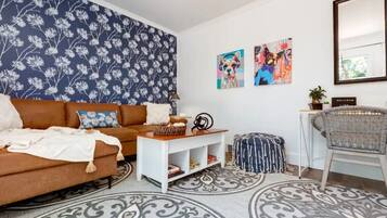 Un salon avec un canapé marron, une table basse blanche, un tapis à motifs et des œuvres d’art murales.