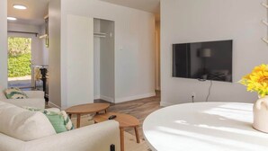 Un salon moderne avec un canapé, une table basse et un téléviseur. Une porte donne accès à une cuisine et à un coin repas.
