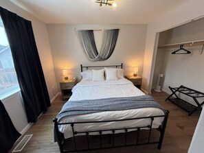 A bedroom with a bed, bedside lamps, a hanging curtain, a radiator, and a coat rack. - Family Getaway - Central Location - No Chores (Anchorage)