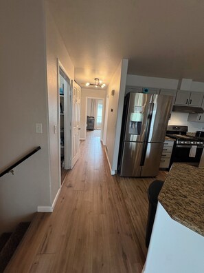 A kitchen with stainless steel appliances, a wooden floor, and a hallway leading to a bedroom. - Family Getaway - Central Location - No Chores (Anchorage)