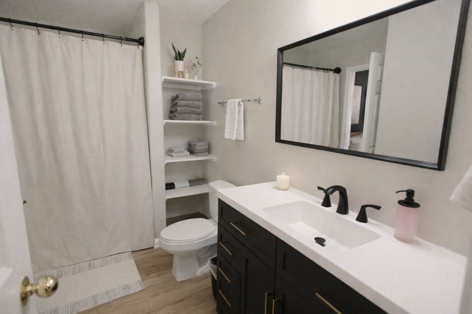 Een badkamer met een witte wastafel, een zwarte kraan, een spiegel, een toilet en planken met handdoeken.