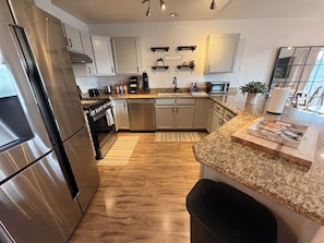 A modern kitchen with stainless steel appliances, granite countertops, and wooden flooring.